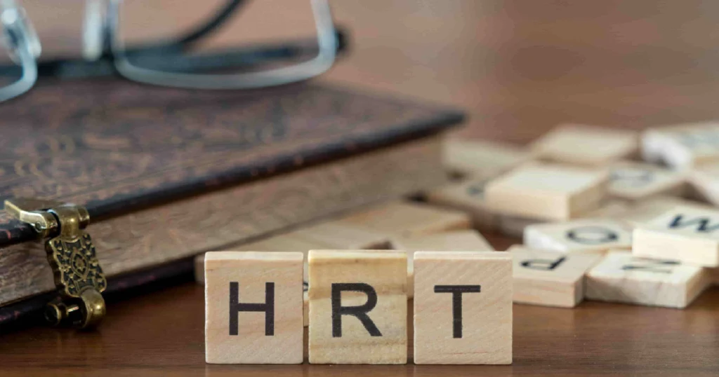 Wooden tiles spelling _HRT_ on a table with book and glasses, symbolizing Hormone Replacement Therapy in Knoxville, TN