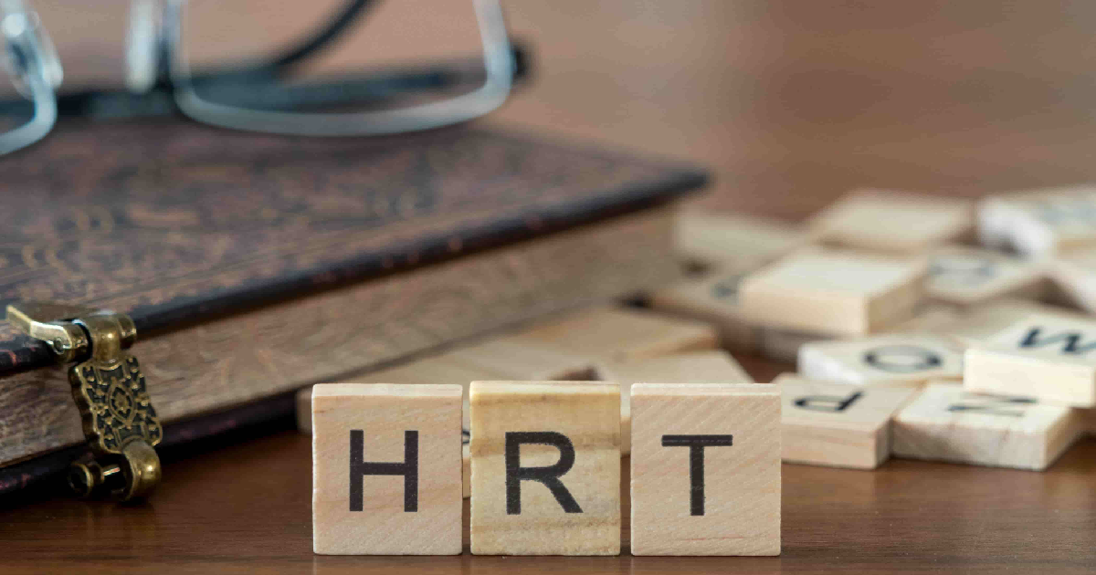 Wooden tiles spelling _HRT_ on a table with book and glasses, symbolizing Hormone Replacement Therapy in Knoxville, TN