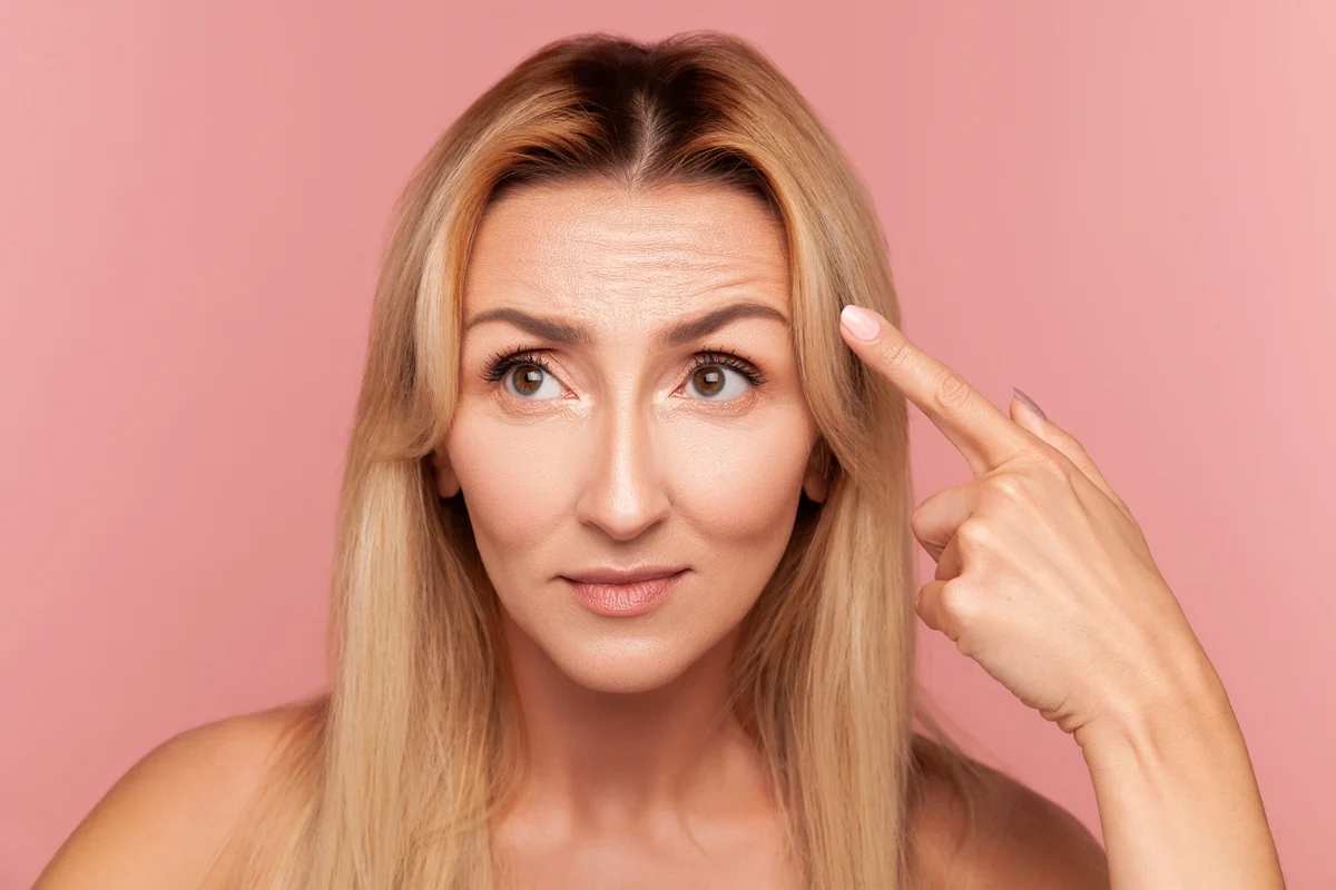 Woman pointing to her forehead while considering Botox for focus and facial lines